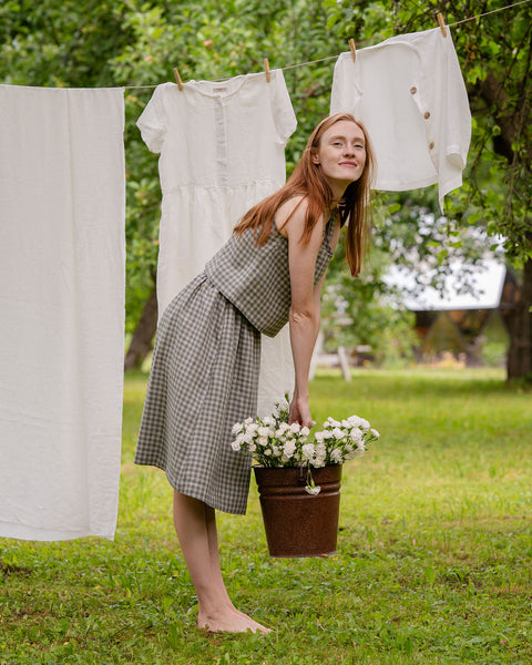 In this picture the model is standing in front of a clothesline with white garments hanging on it. She is holding a metal bucket full of flowers. She is visible full-height, as well as the full skirt length. The skirt is knee length, matched with a same pattern blouse.