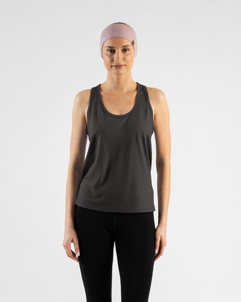 A front view of a blonde woman standing with her arms relaxed at her sides, wearing a charcoal grey tank top, black leggings, and a wide light pink headband against a light grey background.
