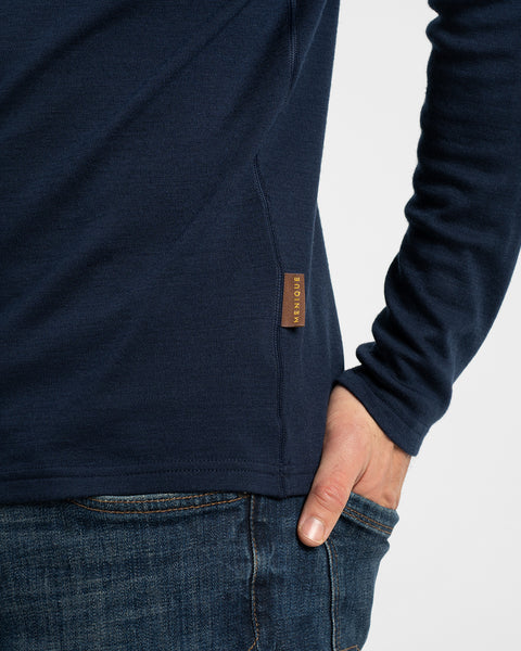 A close-up detail shot of the side hem of a dark navy long-sleeve shirt, highlighting a small brown leather logo tag near the waistline.