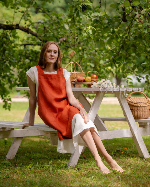 A woman with long reddish-brown hair, wearing a menique linen apron.