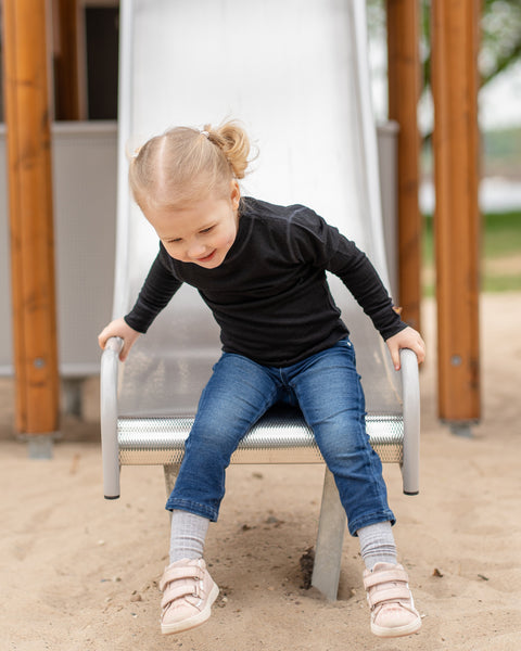 Child sitting on a playground swing set with a slide in the background