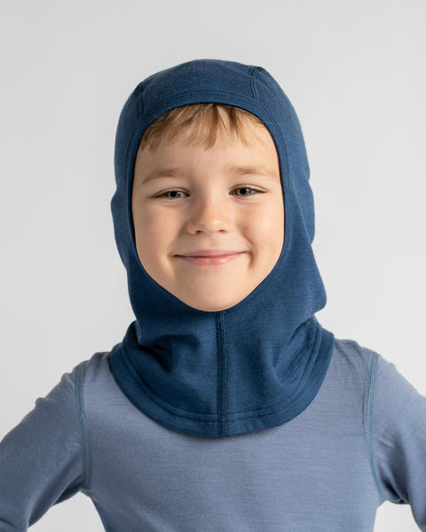 Smiling boy wearing a deep ocean blue balaclava hood matching his light blue thermal top against a plain studio background.