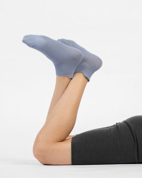 A person lying on their stomach with their lower legs raised, modeling a pair of dusty blue cotton ankle socks.