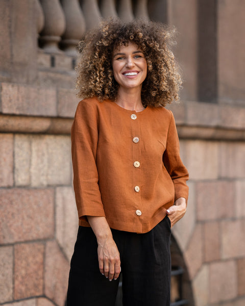 Woman with curly hair wearing almond brown linen jacket Alice and standing in astreet