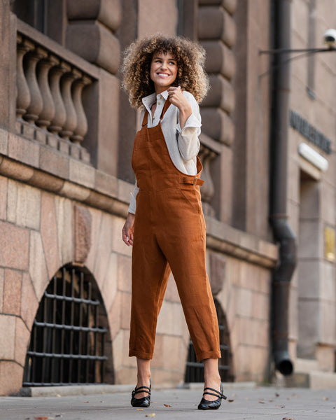 Woman with curly hair standing in a street and wearing Linen Pinafore Jumpsuit Nicci Almond Brown