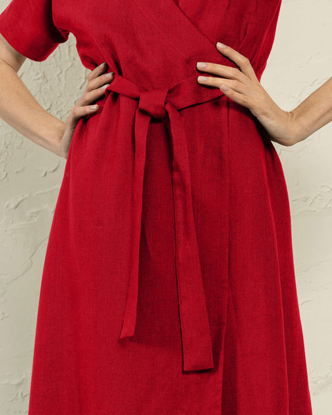 A close-up shot of a person wearing a red dress with a tied belt at the waist. The person's hands are resting on their hips, and the dress is the main focus of the image.