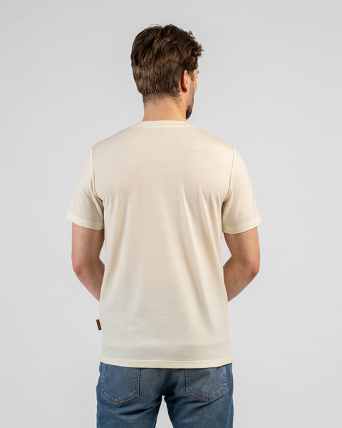 A studio shot showing the back of a man wearing a light beige v-neck t-shirt and blue jeans. He stands facing away from the camera against a plain light grey background.