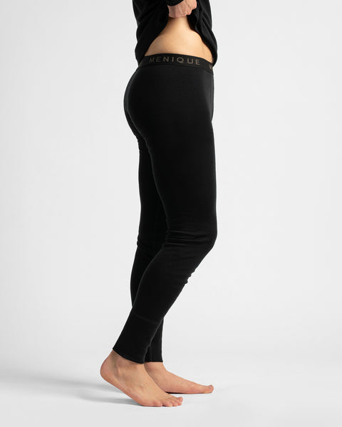 A side profile view of a model wearing black full-length compression leggings with a visible black waistband that reads 'GENIQUE'.