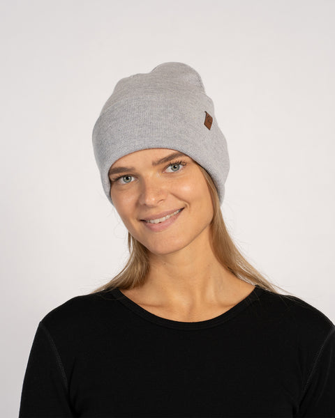 Woman smiling in a light gray knitted merino wool beanie, facing forward in a black top.