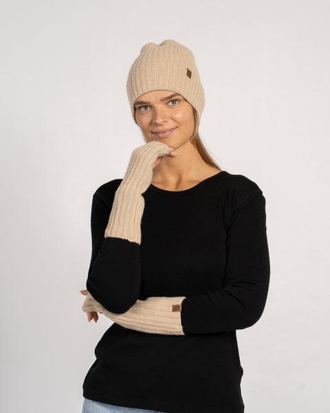 Three-quarter portrait of the model wearing creamy-beige wrist gloves and a matching beanie, arms crossed and smiling slightly.