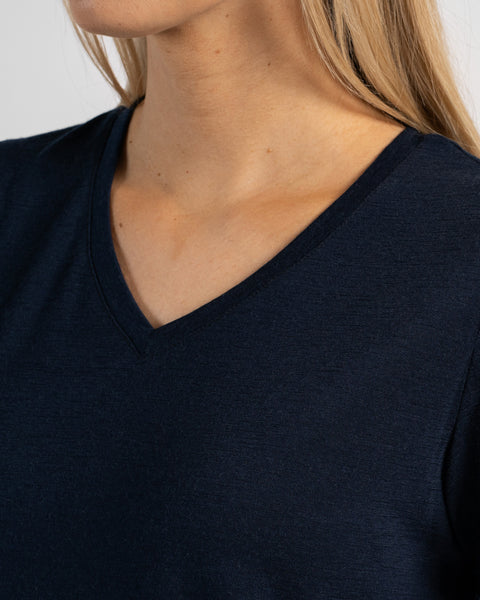 A close-up studio shot focusing on the collarbone area of a woman wearing a dark navy blue short-sleeved V-neck t-shirt against a light grey background.