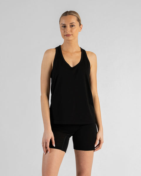 A woman standing straight and facing the camera directly against a white background. She is wearing a black merino sport sleeveless top and black merino slip shorts, with her arms resting casually at her sides.