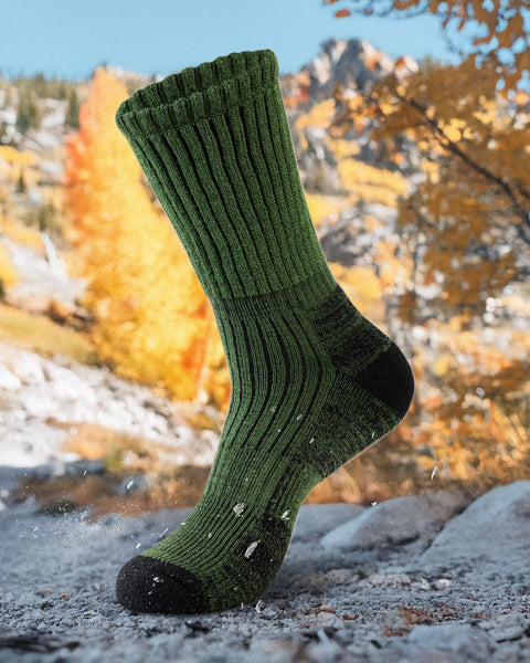 Dark Green sock with black toes and heels on a rocky surface with autumn foliage in the background