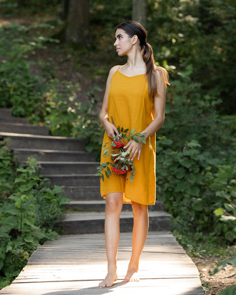 Woman wearing spicy yellow linen dress and standing in the forest