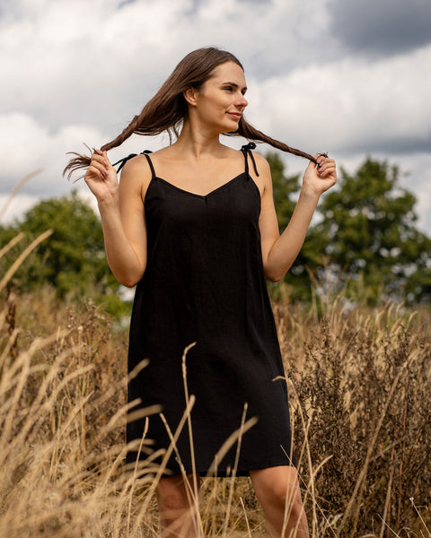 Woman holding her hair and standing outdoors while wearing black midi linen dress