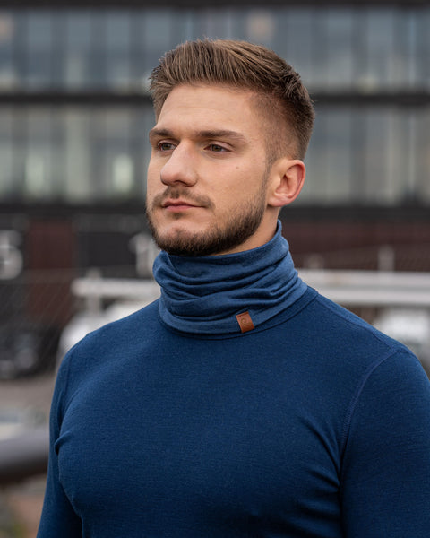 A man wearing the menique unisex denim neck gaiter. He is outside, wearing a matching color long sleeve merino top.