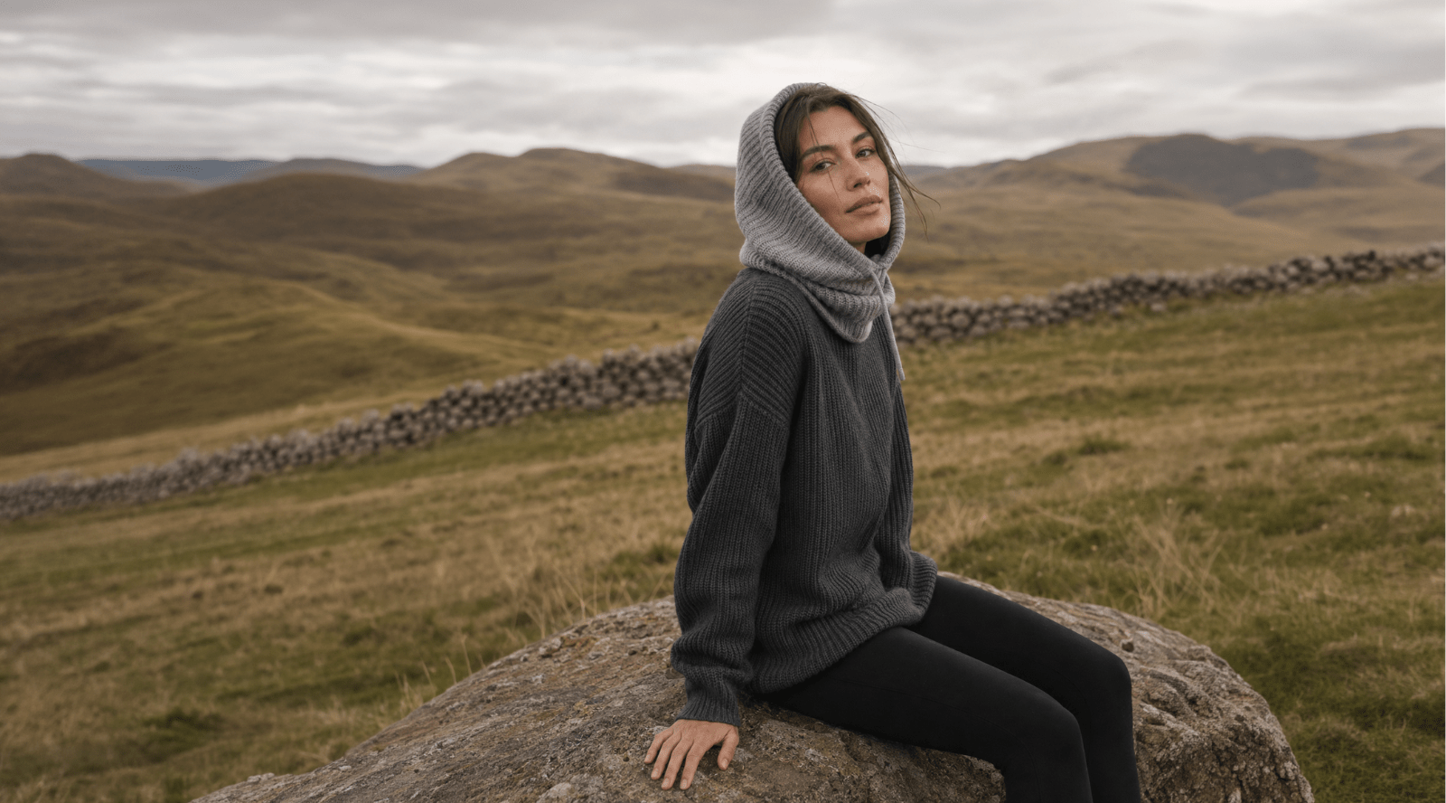 A woman sitting on the rock, looking away into the distance to her left.