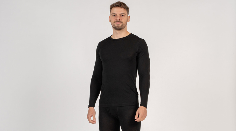 A man wearing all black set of merino wool clothing. These clothing pieces are 160gsm base layers, a long sleeve shirt and pants.