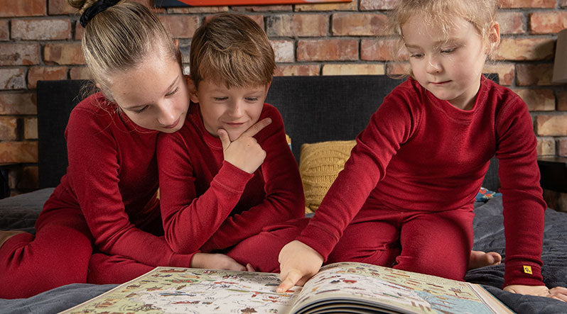 In the photo you can see three little kids looking at the book. They are wearing royal cherry red color matching two-piece sets made from ultra soft and warm 100% Merino wool.