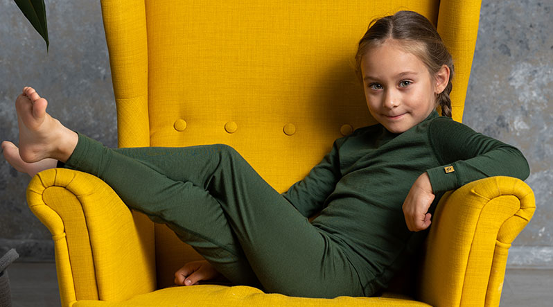 Little girl sitting on yellow armchair and wearing dark green matching set from Merino wool