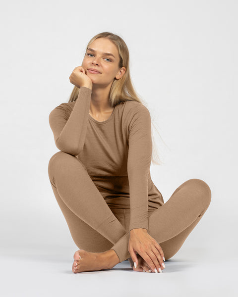 Person wearing a beige merino base layer outfit sitting on a white 
