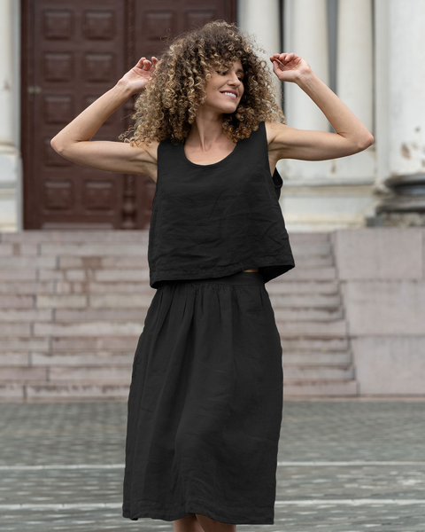 Woman wearing black linen sleeveless top and matching midi skirt, breathable lightweight summer co-ord set with relaxed fit, minimalist sustainable linen outfit styled outdoors
