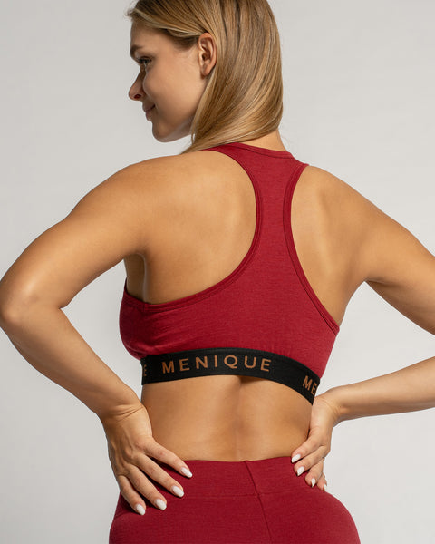 Woman wearing a red sports bra and leggings with &#39;Menique&#39; branding on a light gray background