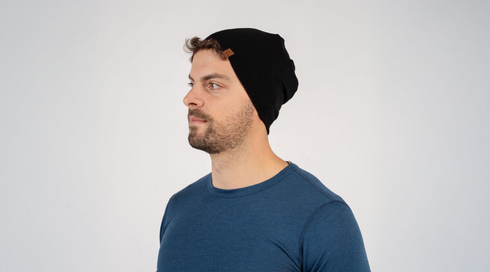 Man wearing a black beanie and blue shirt against a light gray background