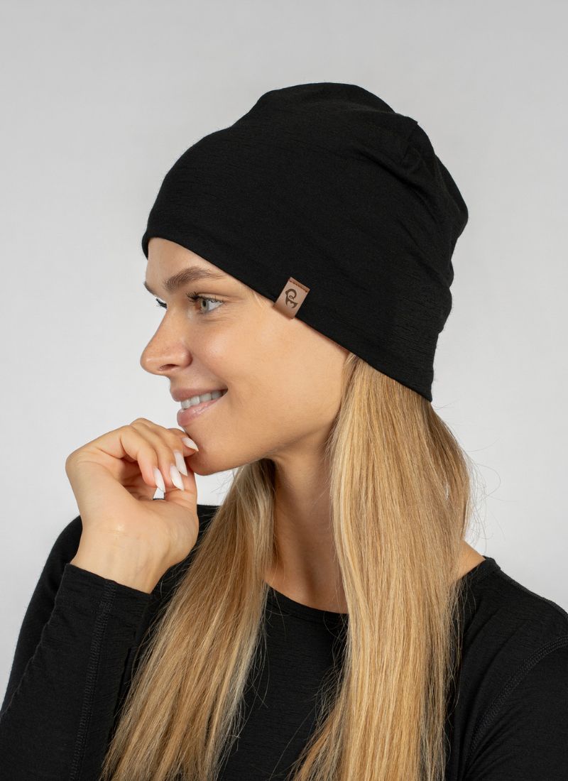Woman wearing a black beanie with a brand logo on a gray background