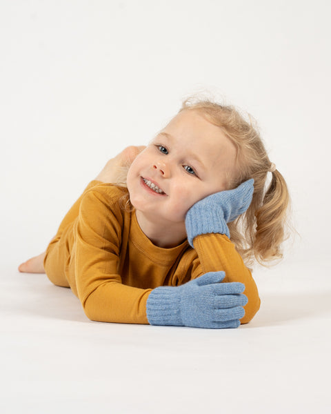 A young child with curly blonde hair and a bright smile wearing light blue gloves on a white background