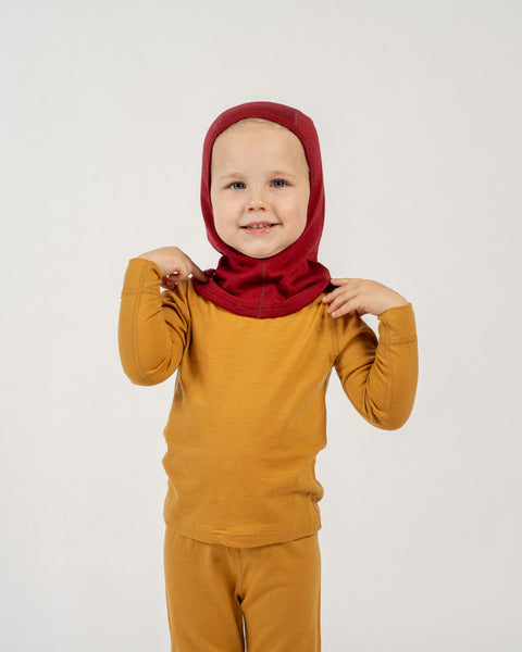 Child wearing a spicy yellow merino outfit with a royal cherry merino balaclava on a white background