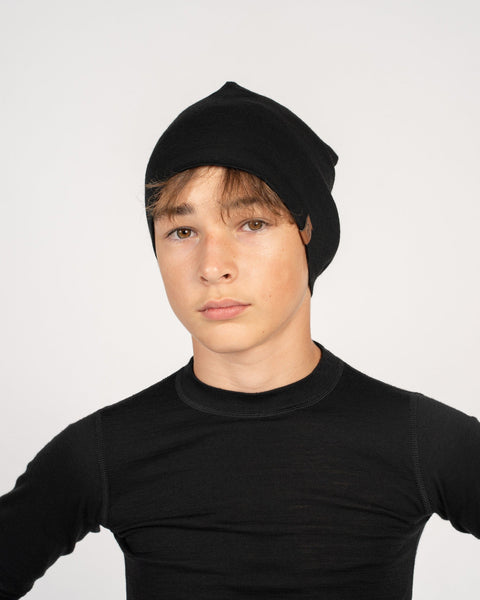 A boy, wearing the menique kids&#39; merino beanie in the color black, dressed n a black long sleeve top as well.