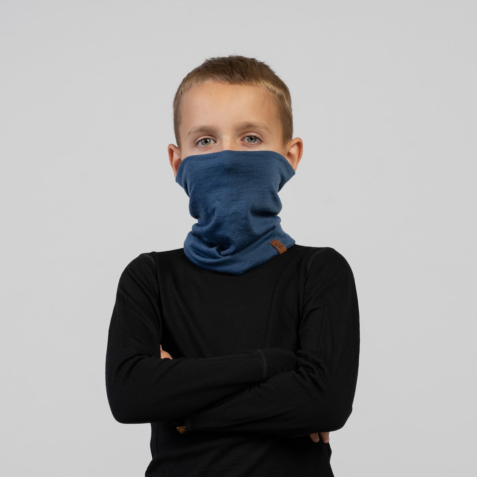 Boy with arms crossed wearing a blue Merino wool neck gaiter – versatile thermal accessory for cold weather.