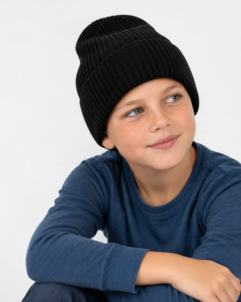 A young boy wearing a ribbed black knit beanie and a long-sleeve blue shirt, looking off to the side against a plain white background.