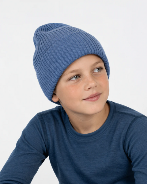 A young boy wearing a ribbed blue knit beanie and a long-sleeve blue shirt, looking off to the side against a plain white background.