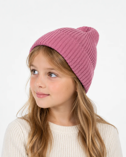 A young girl with long blonde hair wearing a ribbed pink knit beanie and a cream-colored sweater, looking off to the side against a plain white background.