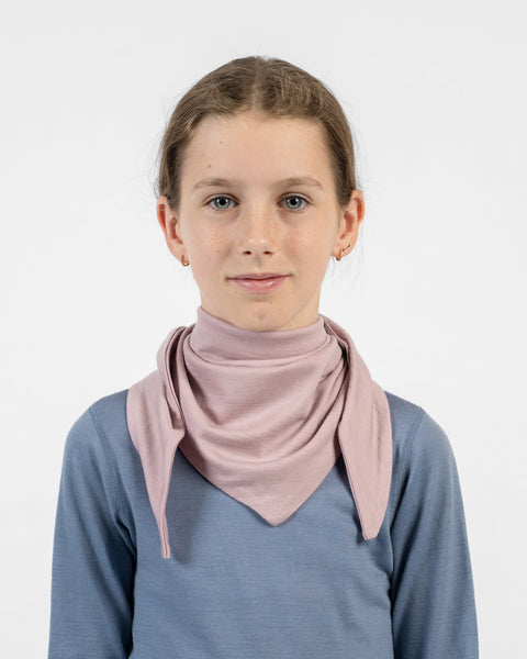 A young girl wearing a dusty pink merino bandana tied around her neck with the triangular point resting on her chest.