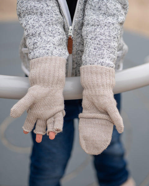 Close-up of child’s hands wearing creamy beige knitted convertible gloves, one mitten flap open showing fingers.