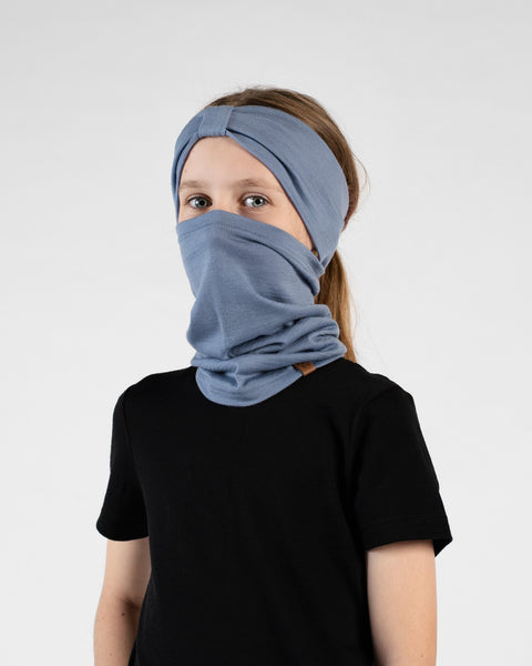 A studio portrait of a young girl looking directly at the camera against a white background. She is wearing a black short-sleeved t-shirt, a dusty blue ribbon headband, and a matching dusty blue neck gaiter pulled up to cover her mouth and nose.