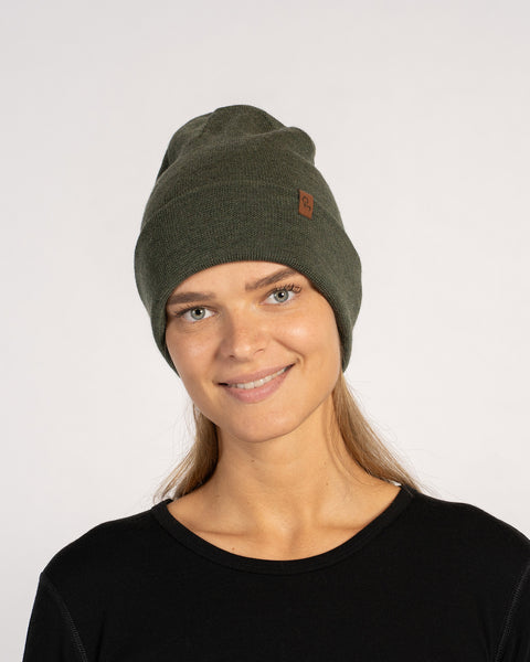 Woman wearing a dark green knitted merino wool beanie, smiling and facing forward in a black top.