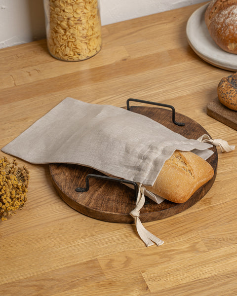 Bread in a reusable fabric bag on a wooden board with a wooden surface background