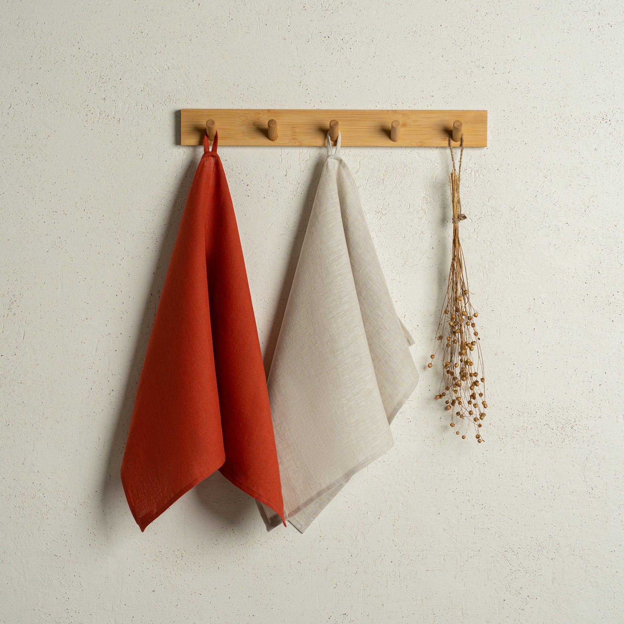 Two menique linen kitchen dish towels hanging on a wooden rack on a wall. The colors of the towels are stone green and green check. 