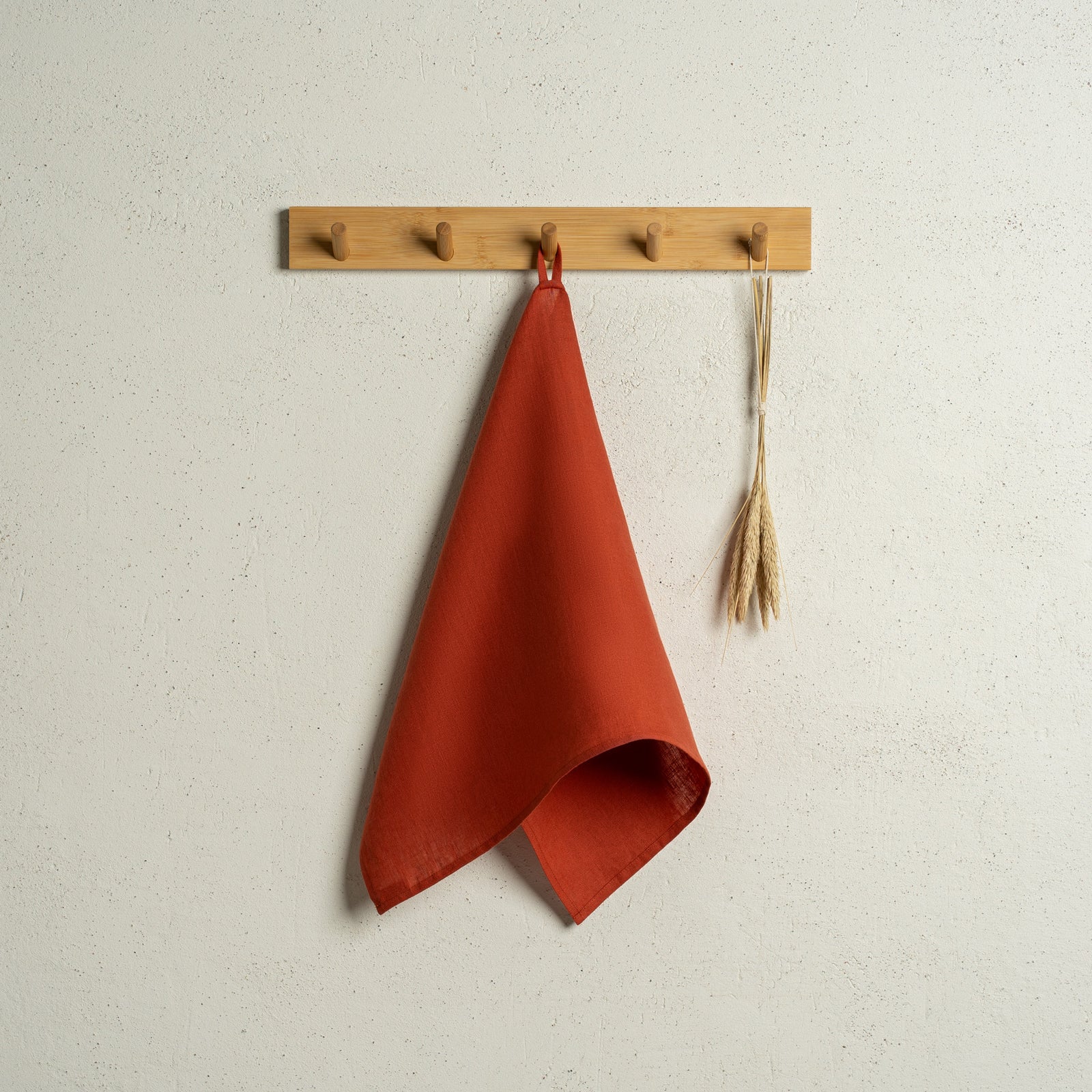 The menique linen kitchen dish towels in the colors of spicy yellow, stone green, natural, cinnamon red, and storm blue hanging on a wooden rack on a wall.