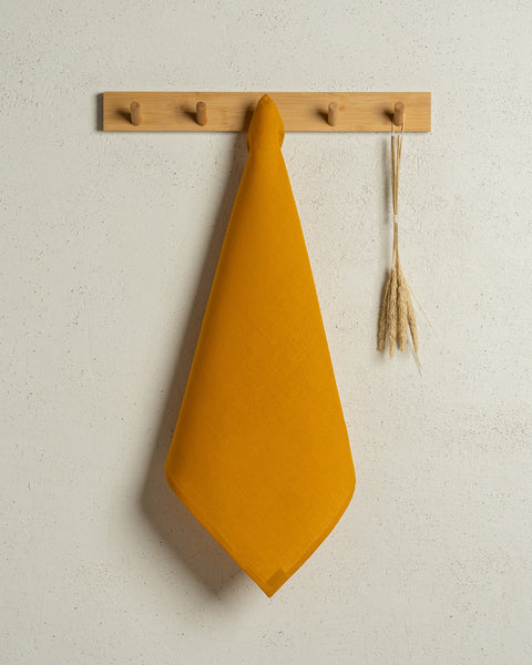 The menique square linen dish towel in color spicy yellow hanging on a wooden rack on a wall.