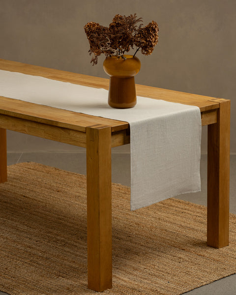 The natural linen table runner on top of a wooden table, captured in a close up picture from the corner of the table. 