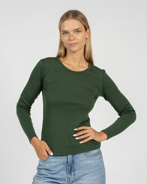 The menique women&#39;s merino wool dark green long sleeve top matched with classic light blue jeans, from the front.