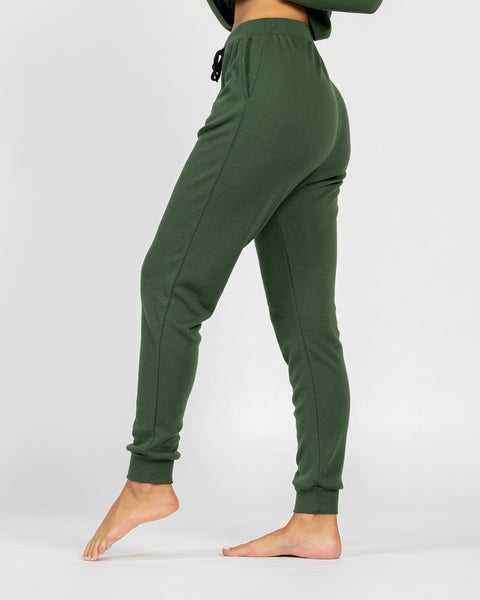 The menique women&#39;s merino wool 250gsm jogger sweatpants in dark green color. They have slightly elastic cuffs by the ankles and an elastic waist. There are visible side pockets.