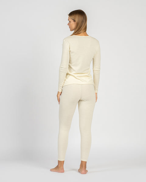 Full-body back view of a woman standing barefoot, wearing a natural cream-colored, long-sleeve base layer top and leggings.