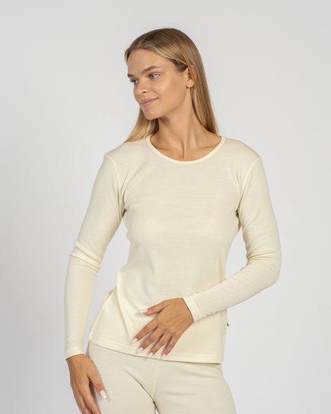 Close-up of a woman looking to her right, modeling a natural cream-colored, long-sleeve base layer top and matching leggings.