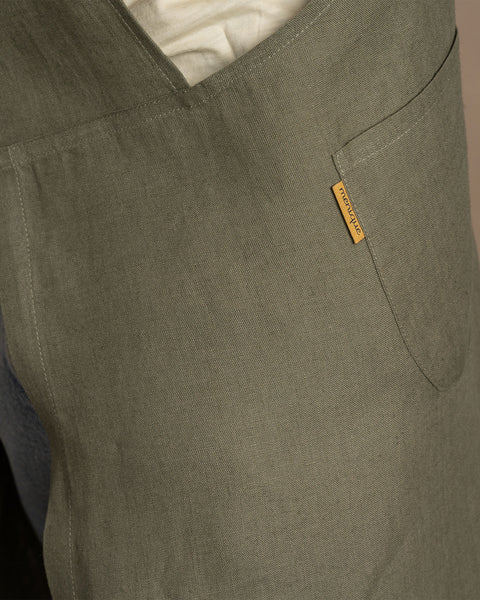 A close-up shot of the textured linen fabric and pocket detail of a stone green menique apron.
